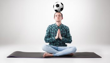 Portrait of young man, practicing yoga with football ball Portrait of young man, practicing yoga with football ball on gray background. concept of continuous soccer practice